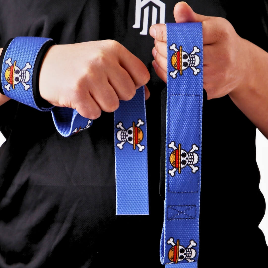 Lifter in a black tee holding the Pirate King weightlifting straps, skull and crossbones repeating down royal blue