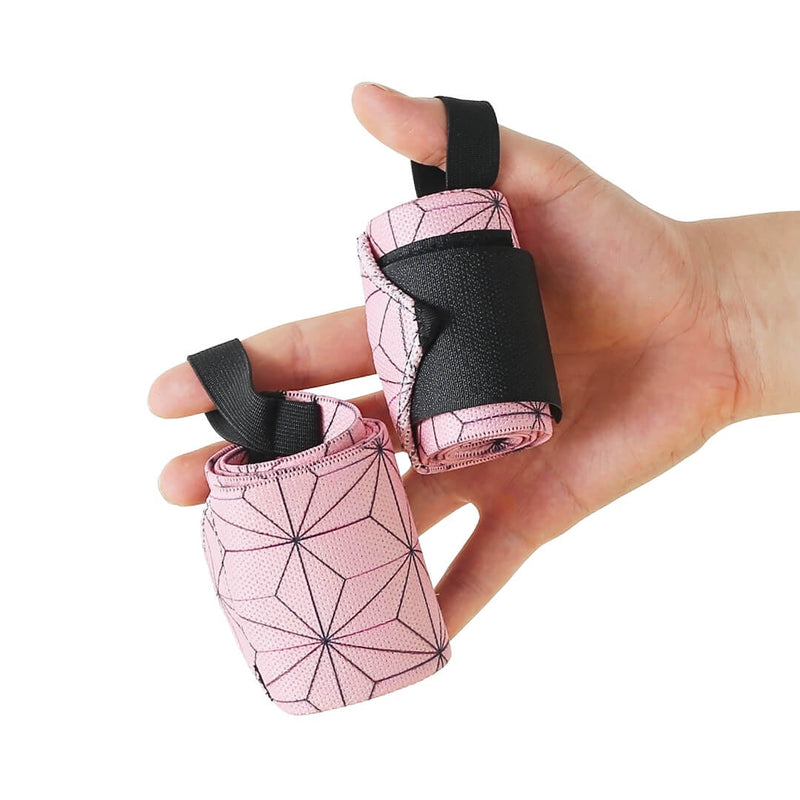 Rolled pair of Asanoha powerlifting wrist wraps held in one hand, pale pink with a dark hemp-leaf star lattice