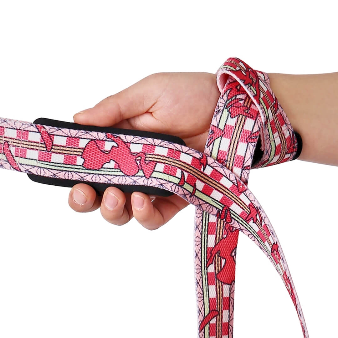 Hand gripping the padded loop of the Kurenai deadlift straps, crimson print on red and white checks over black padding