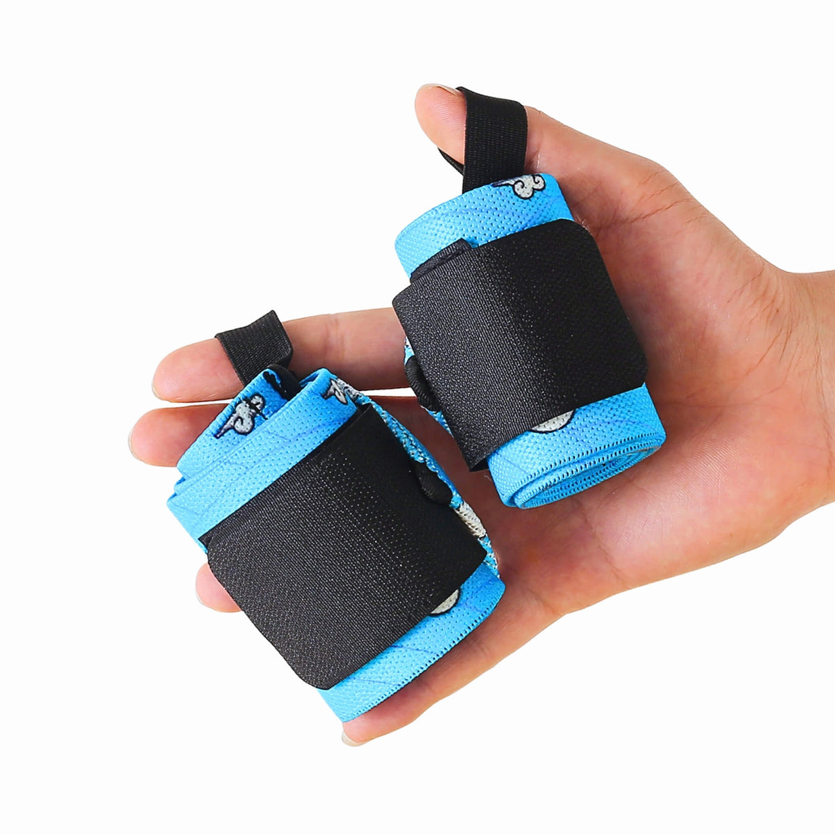 Hand holding a rolled pair of Edo wrist wraps for bench press, sky blue with small white clouds and black closure panels