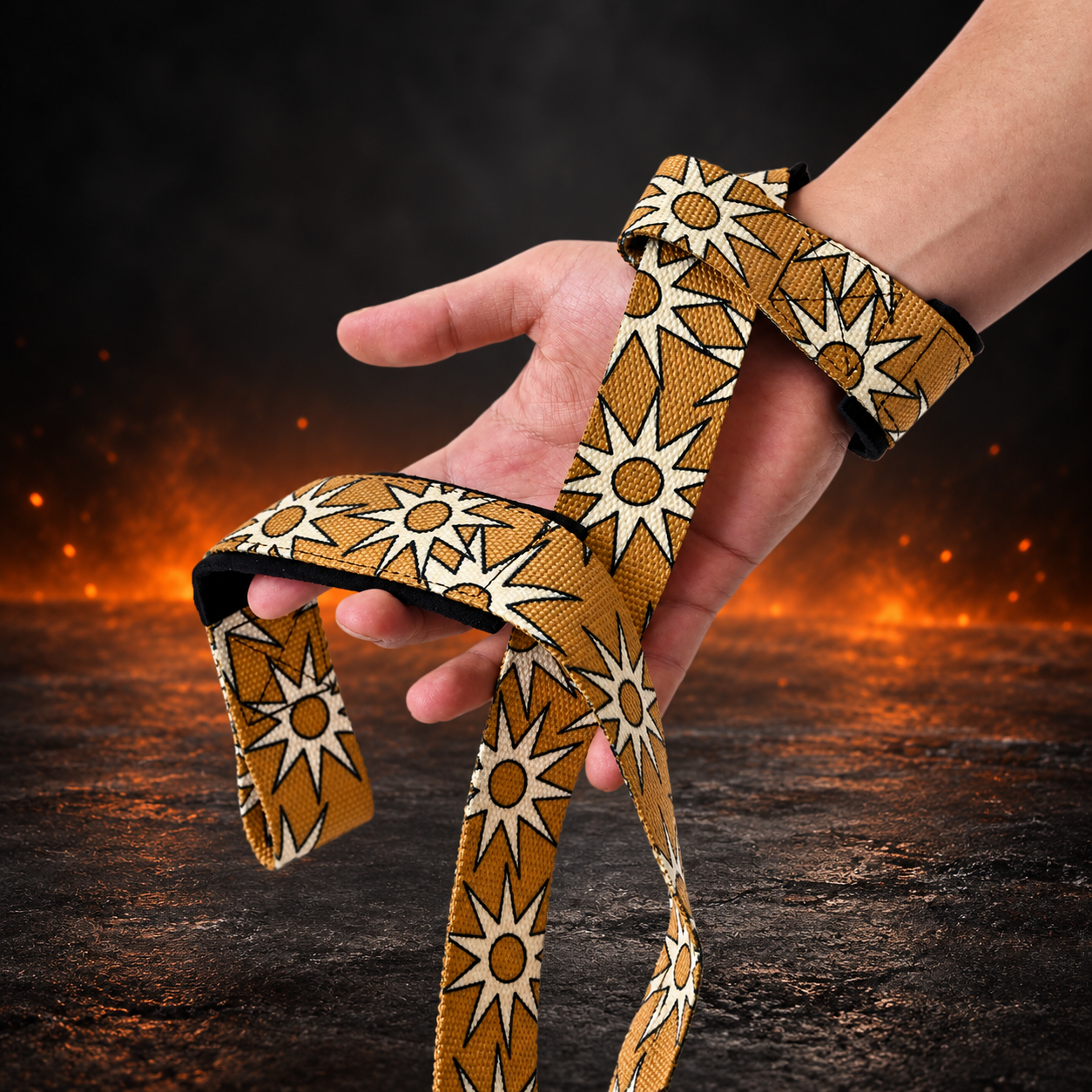 Both Taiyō lifting straps looped over a hand, cream sunbursts with dark outlines repeating on amber webbing