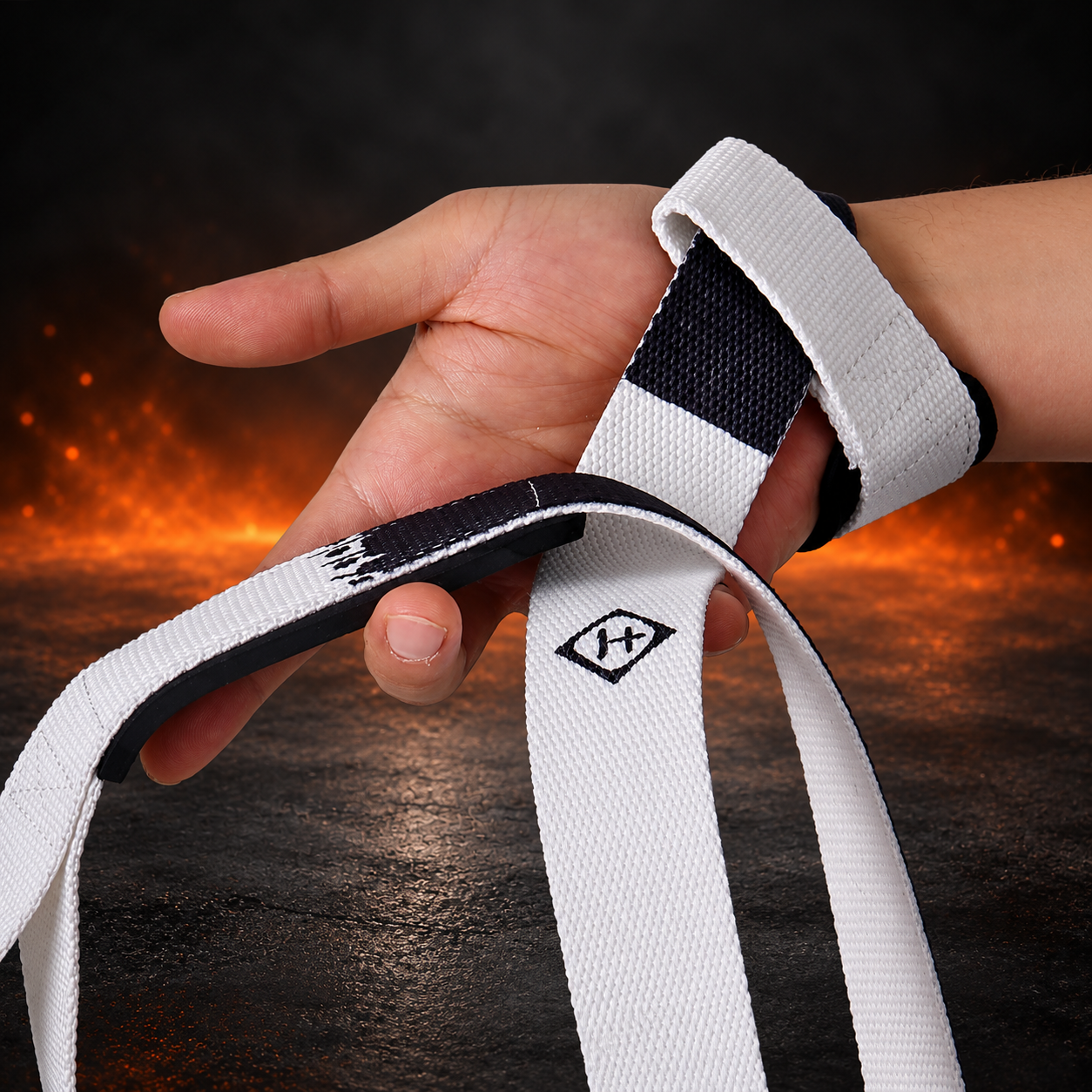 Sumi lifting straps looped on a wrist and around the hand, off-white webbing with a near-black ink band and diamond mark