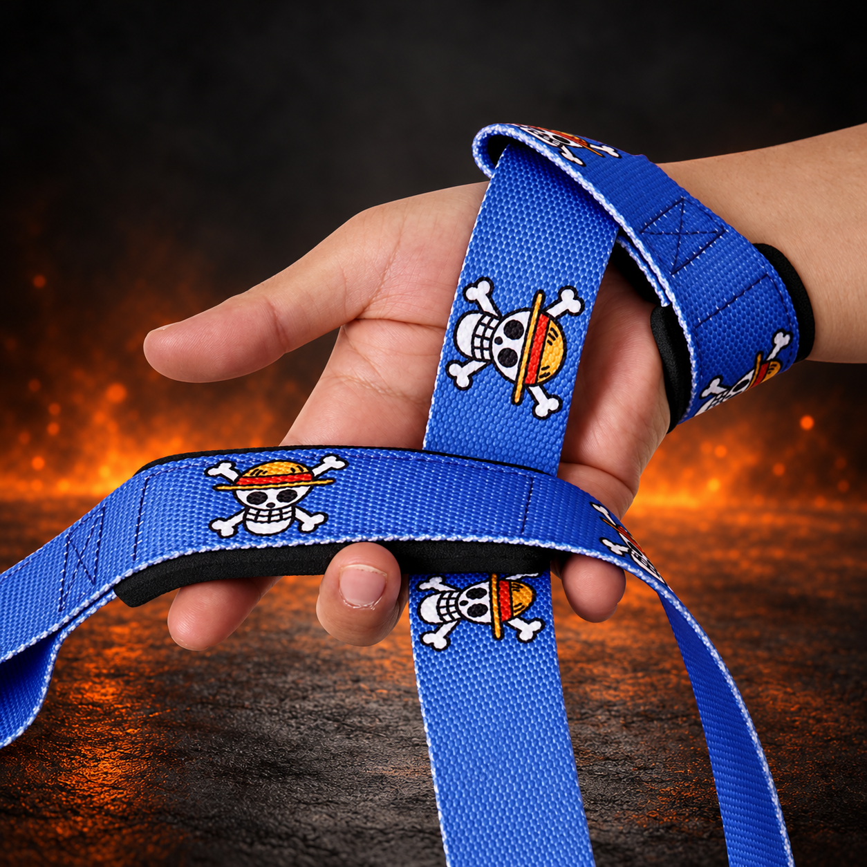 Hand holding the Pirate King lifting straps, one looped at the wrist, royal blue webbing with skulls in red-banded hats