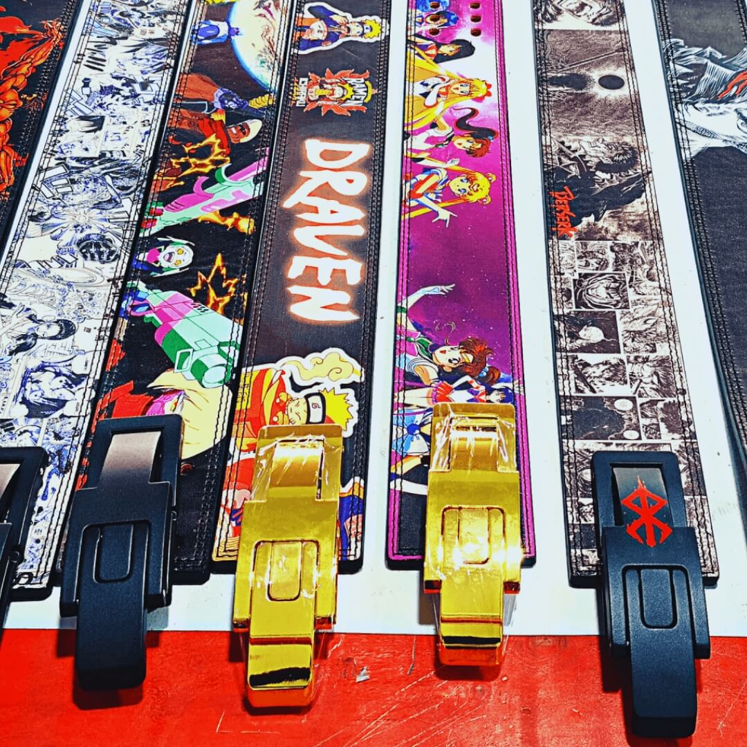 Custom powerlifting lever belts from past orders on a white work table, with black and gold levers.