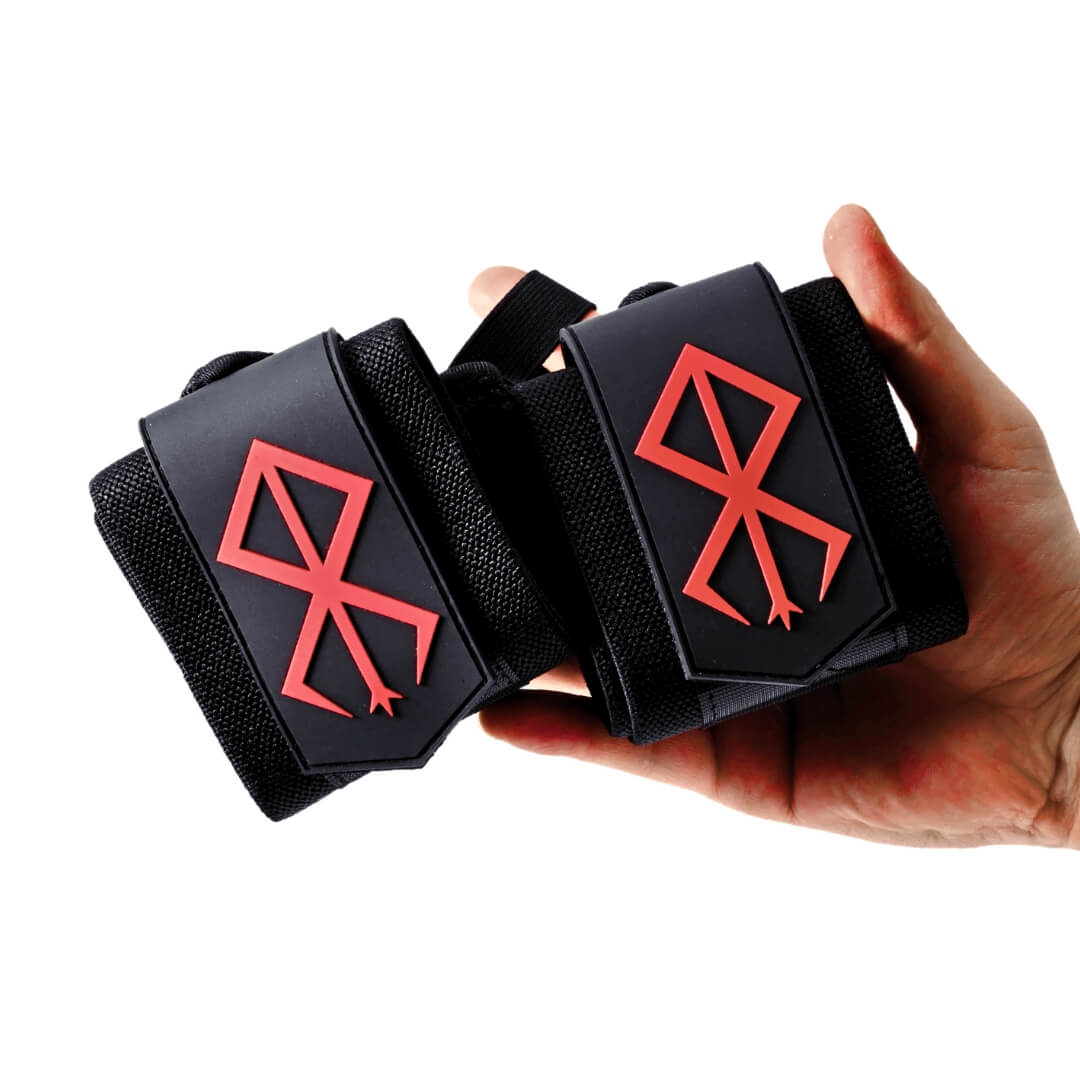 Powerlifting wrist wraps, rolled black pair with red sigils resting in an upturned hand.