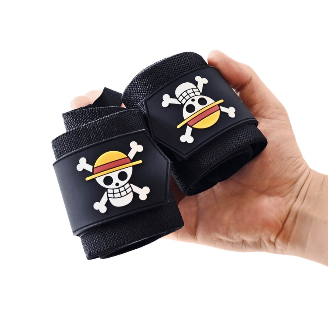 Powerlifting wrist wraps, rolled black pair with skull and crossbones patches resting in an open hand.