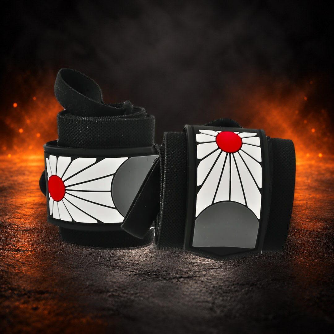 Powerlifting wrist wraps, rolled black pair with red sun panels, one thumb loop raised, angled view.