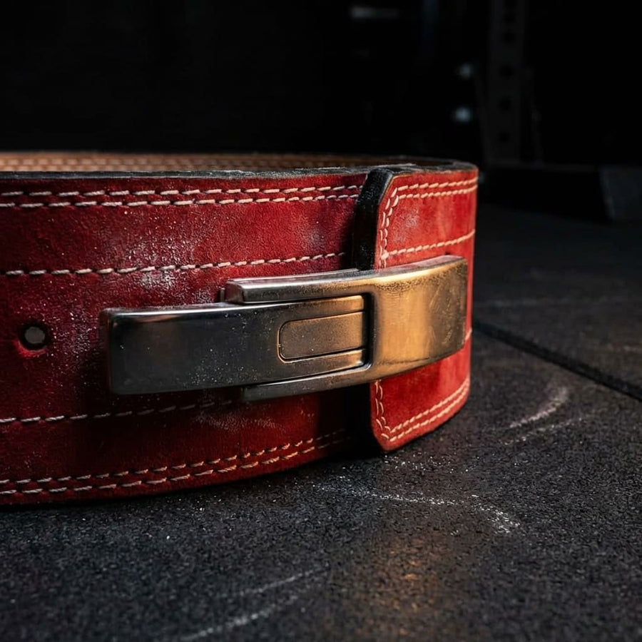 Close-up of a red leather powerlifting belt with a metal buckle on a dark surface