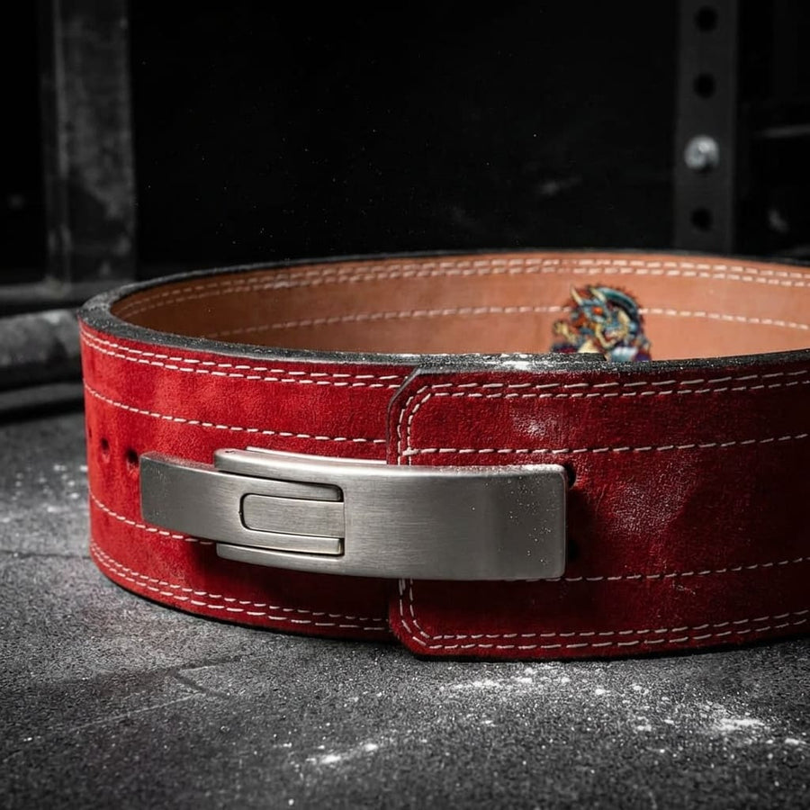Red leather weightlifting lever belt with a silver buckle on a dark surface